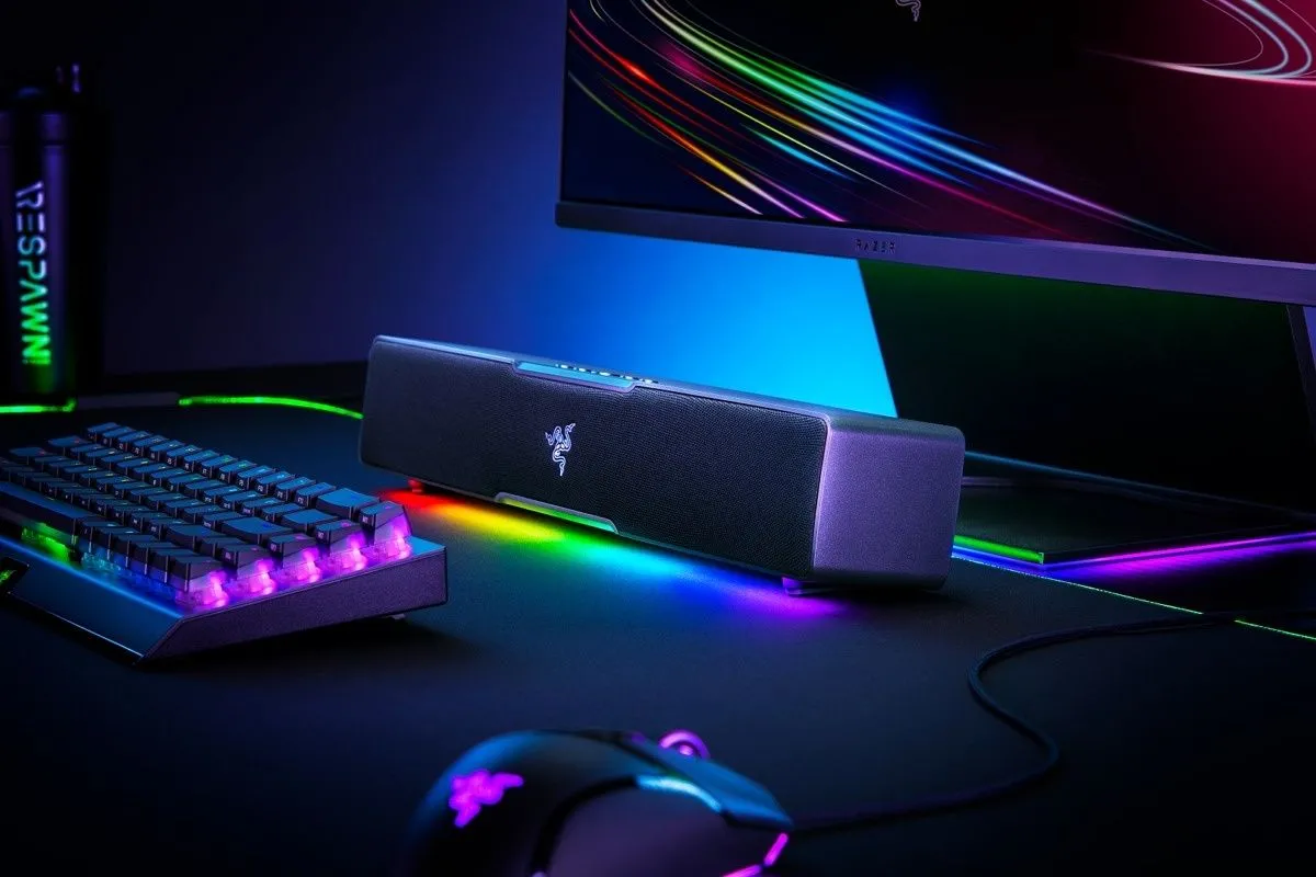 Soundbar Razer Leviathan V2 X với đèn RGB sáng, đặt cạnh bàn phím, chuột và màn hình trong góc gaming PC