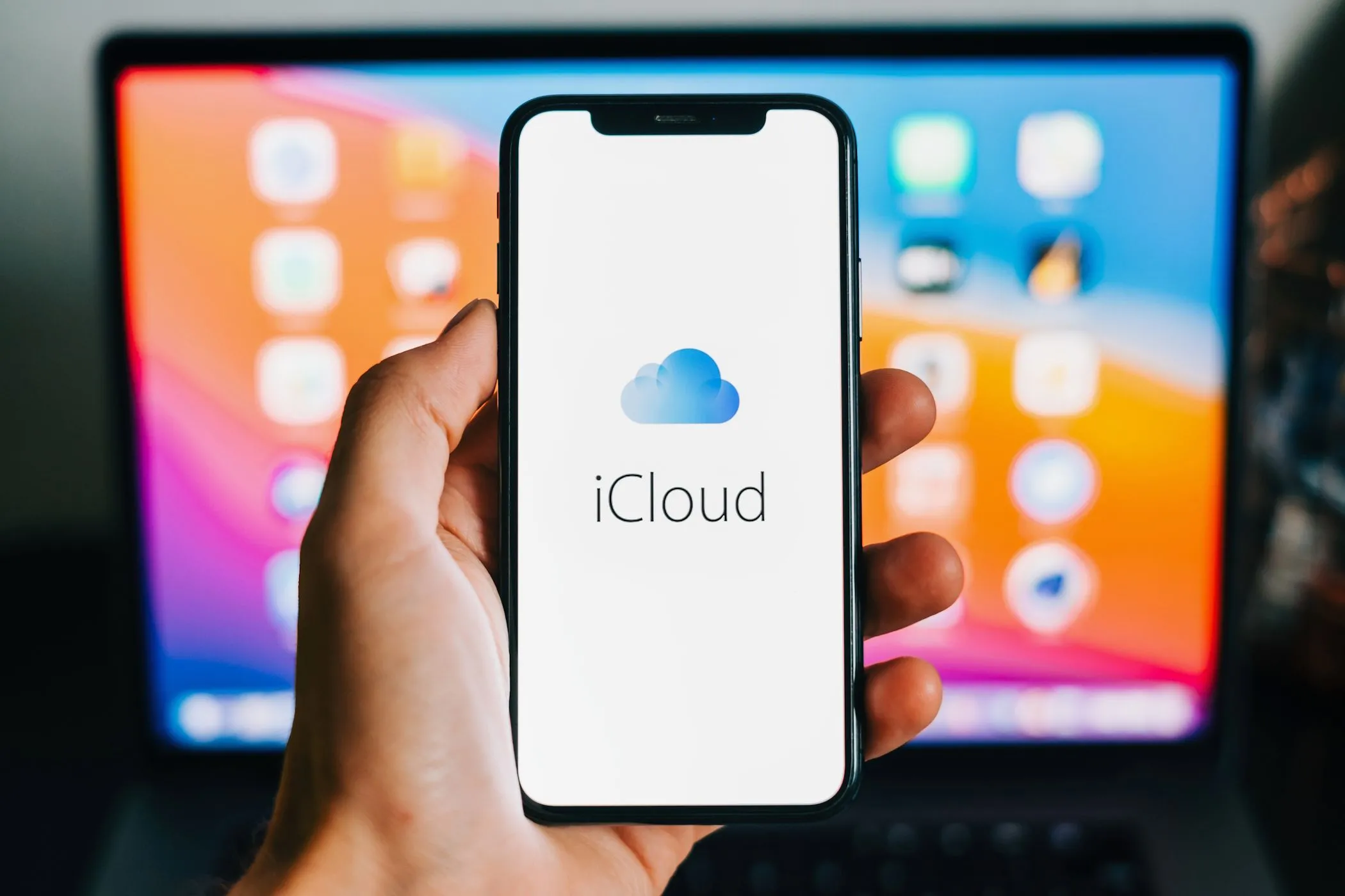 Biểu tượng iCloud hiển thị trên iPhone với MacBook ở nền