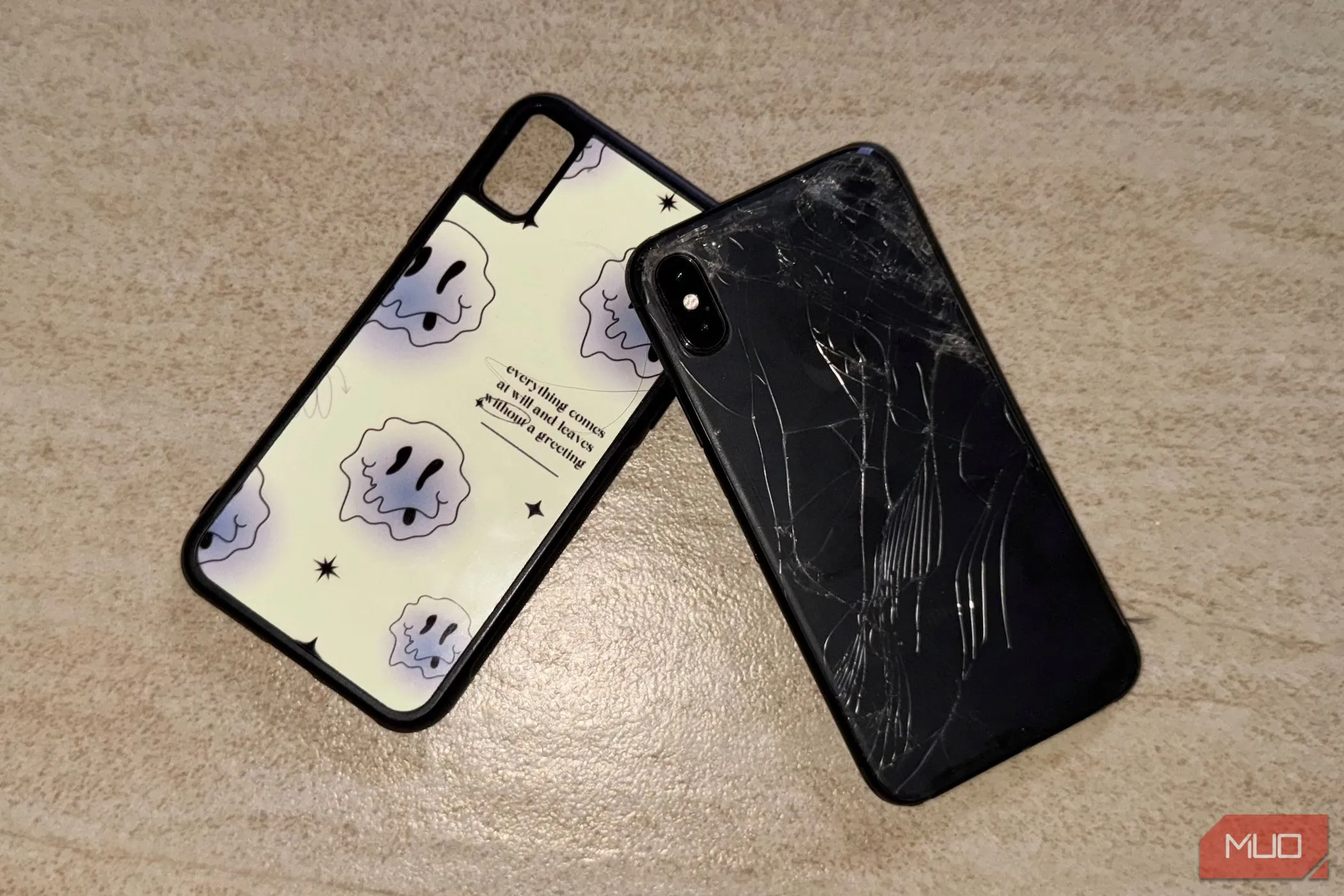 Chiếc iPhone X với mặt lưng kính bị nứt nằm trên sàn nhà cạnh ốp lưng điện thoại.