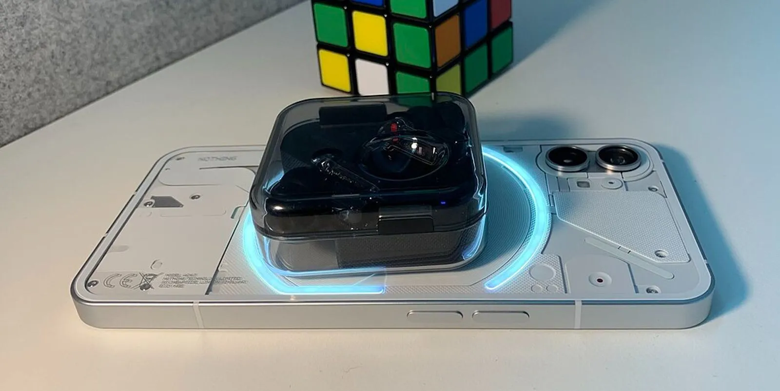 Điện thoại Nothing Phone (1) đang sạc không dây cho tai nghe, đặt phía trước một khối Rubik, minh họa tính năng sạc ngược.