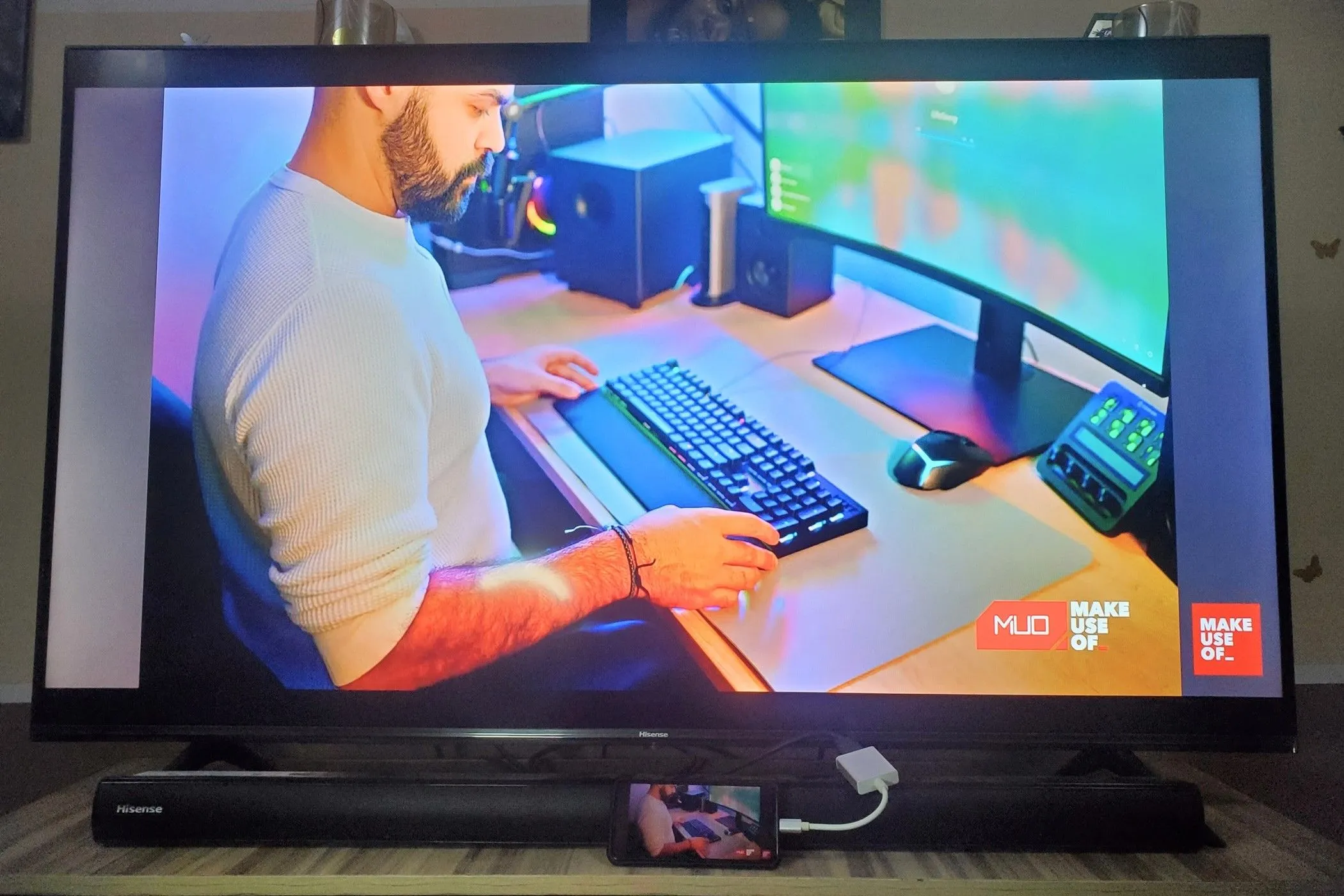 Điện thoại thông minh kết nối với TV qua adapter USB-C sang HDMI, hiển thị giao diện Samsung DeX và một người đàn ông đang làm việc với bàn phím