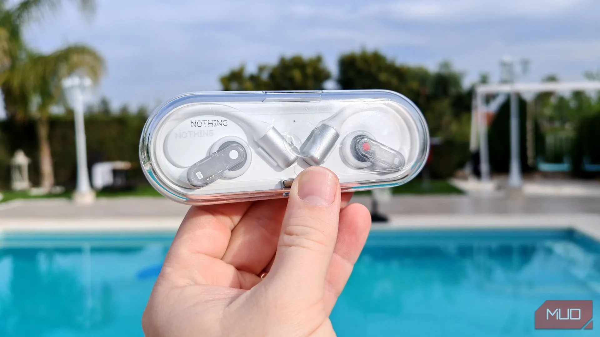 Hộp sạc Nothing Ear (open) với thiết kế trong suốt, được cầm trên tay ở ngoài trời, thể hiện tính di động và phong cách.