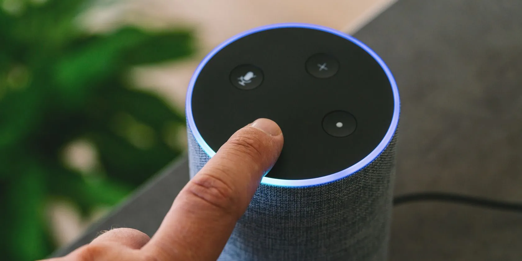 Loa thông minh Amazon Echo màu đen đặt trên bàn, phía sau là hình ảnh mờ của một người, minh họa thiết bị trợ lý giọng nói trong môi trường gia đình.