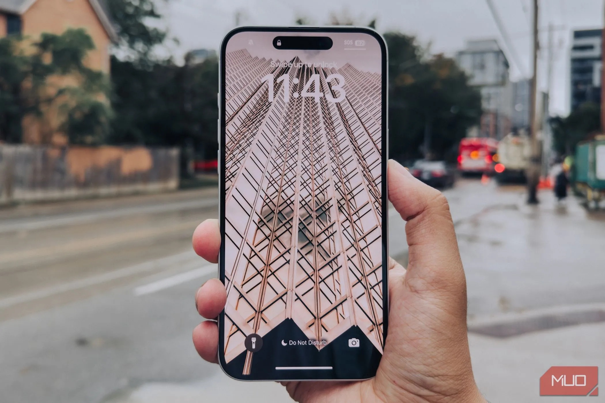 Màn hình của iPhone 16 Plus với viền mỏng được cầm trên tay trước phông nền thành phố.