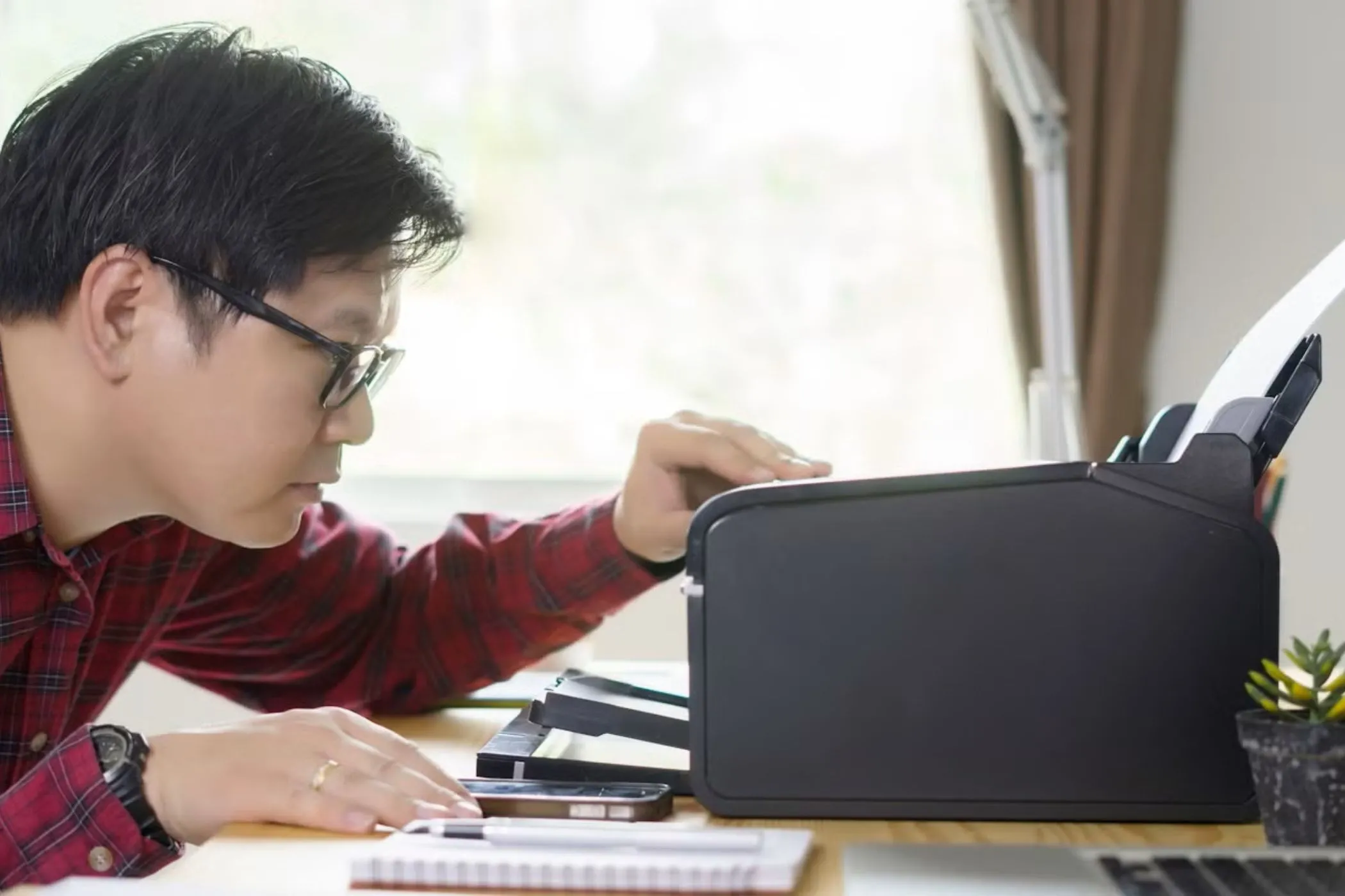 Một người đàn ông đang nhìn vào máy in trên bàn, minh họa vấn đề tương thích với thiết bị ngoại vi trên Chromebook.