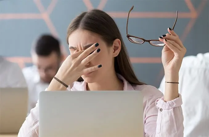 Một phụ nữ đang xoa mắt, biểu hiện của tình trạng mỏi mắt do sử dụng thiết bị điện tử trong thời gian dài.