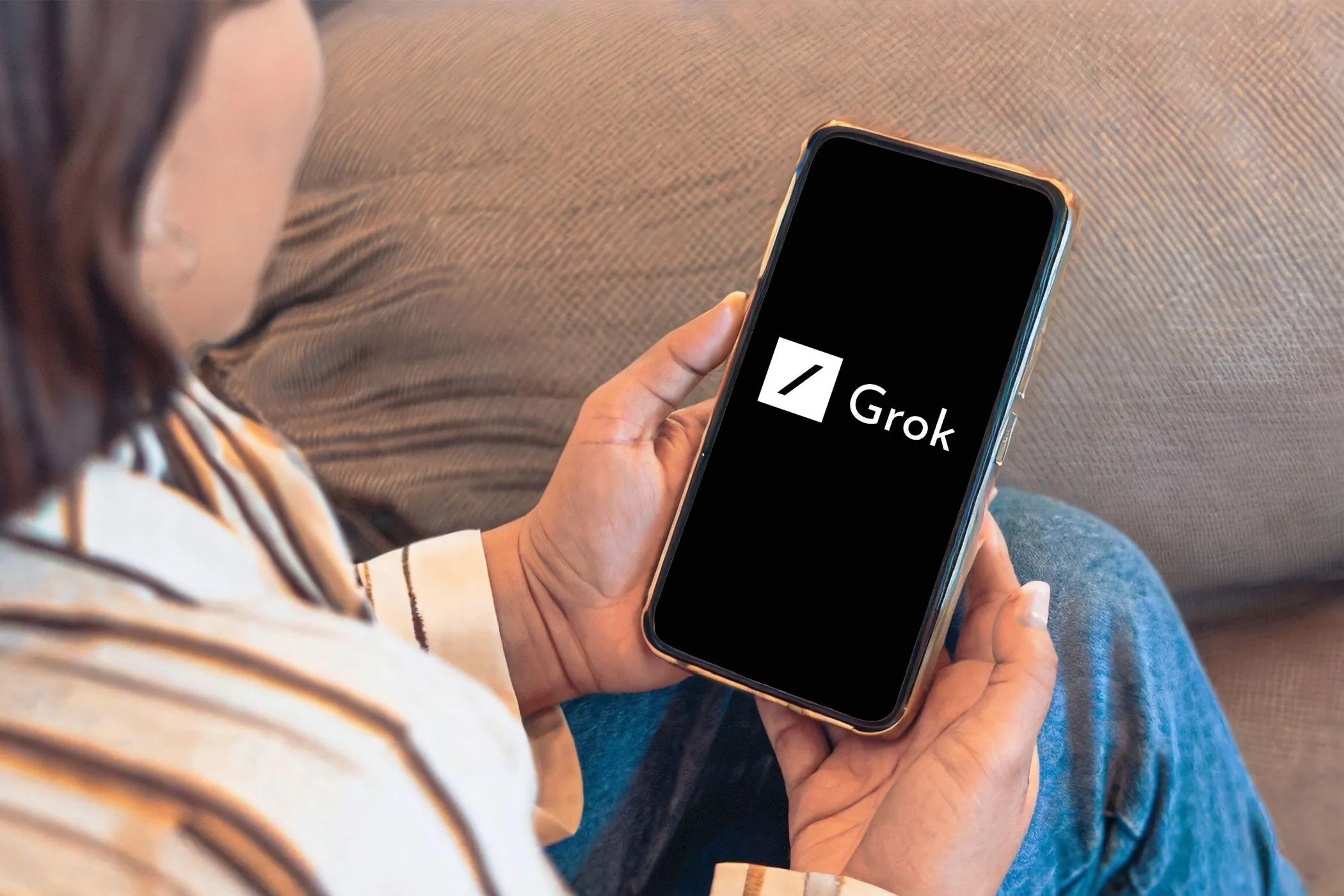 Người dùng đang xem điện thoại với logo Grok AI trên màn hình, thể hiện sự tương tác với công cụ trí tuệ nhân tạo Grok.